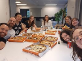 People smiling at camera, many pizzas on the table